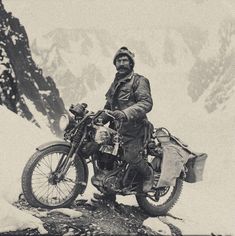 an old black and white photo of a man on a motorcycle in the snow with mountains behind him