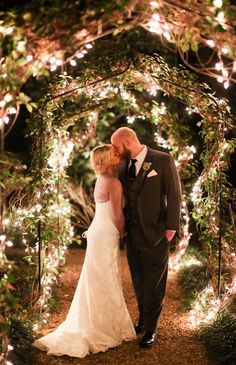 a bride and groom kissing under an archway covered in fairy lights