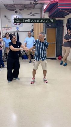 two people are dancing in an empty room with other people standing around and talking to each other