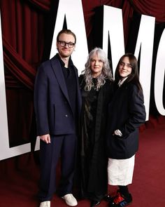 two people standing next to each other in front of a red curtain and the word mom written on it