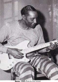 a black and white photo of a man playing an electric guitar with stripes on his pants