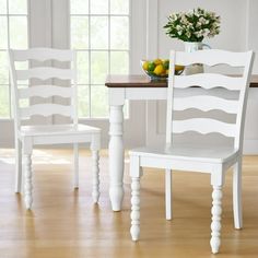 two white chairs sitting at a table with fruit on the table and windows in the background