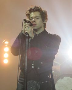 a man holding a microphone while standing on top of a stage with lights behind him