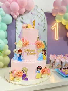 there is a pink cake with princess figures on it and balloons in the back ground