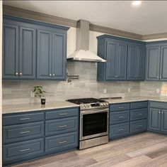 a large kitchen with blue cabinets and stainless steel stove top oven, range hood, and dishwasher