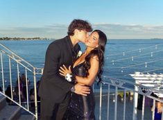 a man and woman standing next to each other in front of the ocean with their arms around each other