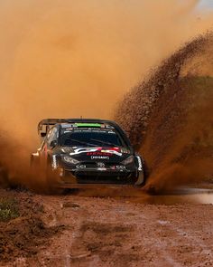 a car is driving through the mud on a dirt track with dust coming off it's tires