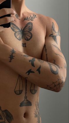 a shirtless man holding a cell phone in his right hand and tattoos on his left arm