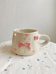 a cup with pink bows on it sitting on top of a white cloth covered table