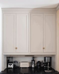 a kitchen with white cupboards and black counter tops in front of a wall mounted coffee maker