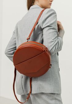 Introducing our premium handcrafted round crossbody bag designed for the modern woman. This sophisticated bag blends style and functionality, making it the perfect accessory for both daily and evening use. Key Features: Spacious Interior: Generously accommodates your essentials, including a small tablet or document folder. Organized Storage: Features one large compartment, a dedicated pocket with a strap and button closure, and two patch pockets. Secure Closure: Equipped with a sturdy zipper for added security. Versatile Carrying Options: Includes a long shoulder strap for convenience. Durable Material: Crafted from wear-resistant natural crust leather in a dark beige color. Quality Lining: The interior is lined with high-quality textile material. Elegant Details: Adorned with a small name Brown Backpack, Designer Backpack, Brown Backpacks, Round Bag, Backpack Straps, Designer Backpacks, Backpack Purse, Baby Bag, Women's Bags