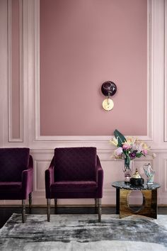 two purple chairs sitting next to each other in front of a wall with pink walls