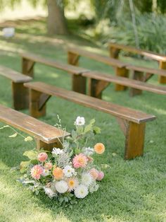 a bunch of wooden benches sitting on top of a grass covered field next to flowers