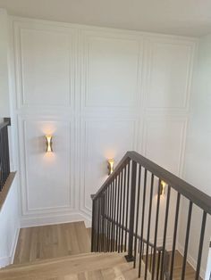 an empty room with white walls and wooden floors, two lights on the wall above the stairs