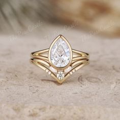 a gold ring with a pear shaped diamond in the center, on top of a rock