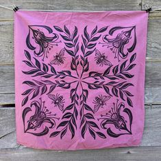 a pink wall hanging with black and white designs on it's side, along with a wooden fence