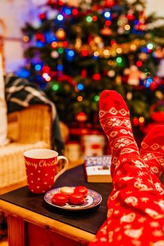 a woman's feet with red socks and christmas stockings on, next to a cup of coffee