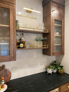 a kitchen with wooden cabinets and marble counter tops, filled with wine glasses on the shelves