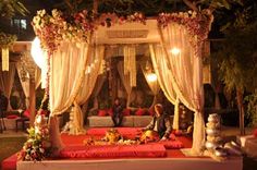 a man and woman sitting on a couch under a canopy covered in flowers, surrounded by candles