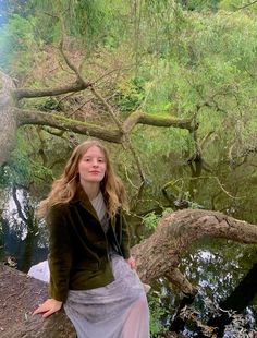 a woman sitting on top of a tree branch next to a body of water with trees in the background