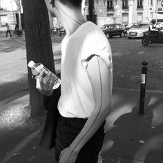 a man standing next to a tree holding a water bottle in his hand and listening to headphones