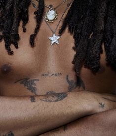 a man with dreadlocks and a star pendant on his chest is looking at the camera