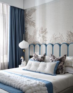 a white bed with blue trim and pillows in a bedroom next to a curtained window