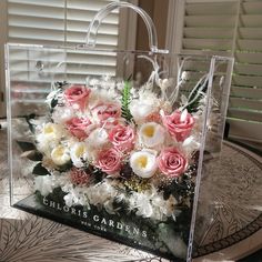 a clear bag with pink and white flowers in it sitting on a table next to a window