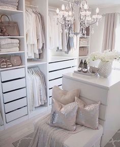 a white closet with chandelier, pillows and shoes on the floor in front of it