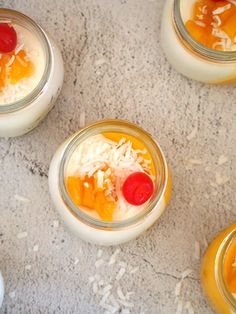 four desserts in small glass jars with fruit on the top and coconut flakes