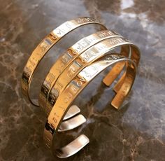 a gold cuff bracelet with five different types of coins on the inside and outside, sitting on a marble surface