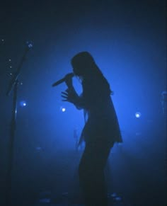 a woman standing in front of a microphone on stage with blue lights behind her and one arm raised up