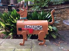 a cardboard dog mailbox sitting on top of a sidewalk next to a planter