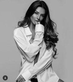 a woman posing with her hands on her face and looking at the camera while wearing a white shirt