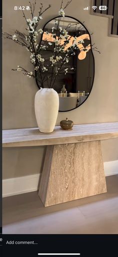 a vase with flowers sitting on top of a wooden table in front of a mirror