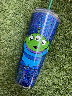 a blue and green cup with a cartoon character on it sitting in the grass next to a straw