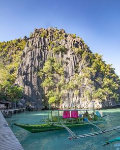 two boats docked at the end of a pier in front of a large rock formation