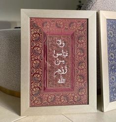 two framed pictures sitting on top of a table next to each other with arabic writing