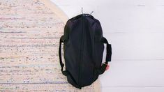 a black backpack sitting on top of a rug next to a white wall and floor