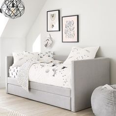 a bedroom with white walls and flooring has a gray daybed in the corner