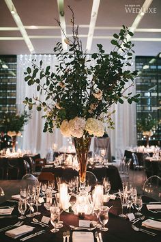 a vase filled with white flowers sitting on top of a table covered in glasses and plates