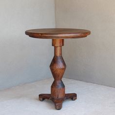 a small wooden table sitting on top of a white floor next to a gray wall