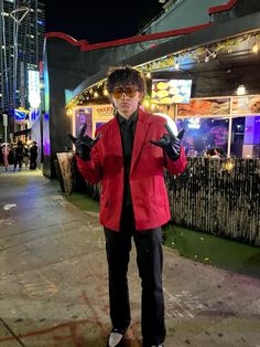 a man in a red jacket and black pants standing on the sidewalk with his hands up