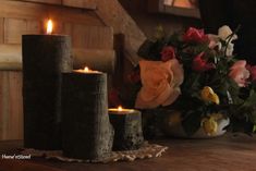 two candles sitting on top of a wooden table with flowers in the vase behind them