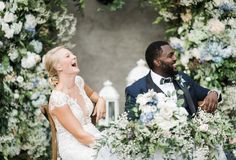 a man and woman sitting at a table with flowers in front of them, laughing