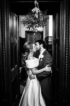 a bride and groom kissing in an open doorway at their wedding reception, black and white photo