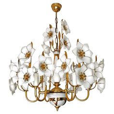 a chandelier with white flowers hanging from it's center and gold accents