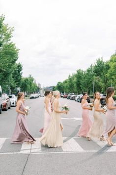 the bridesmaids are crossing the street in their dresses, and one is holding her bouquet