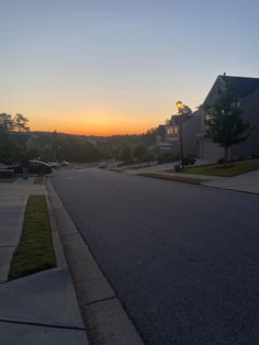 the sun is setting on an empty street with houses in the background and cars parked along the curb