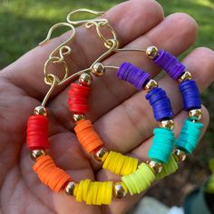 a person is holding some colorful beads in their hand and wearing gold earrings